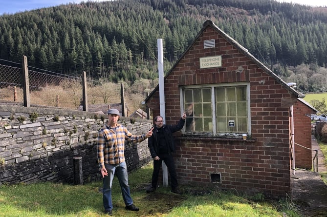 David Evans and Gareth Donovan point at telephone exchange in Corris after internet went down for two weeks due to Storm Eunice. 