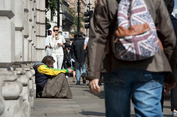 Members of the public walk past a homeless man begging in central London.