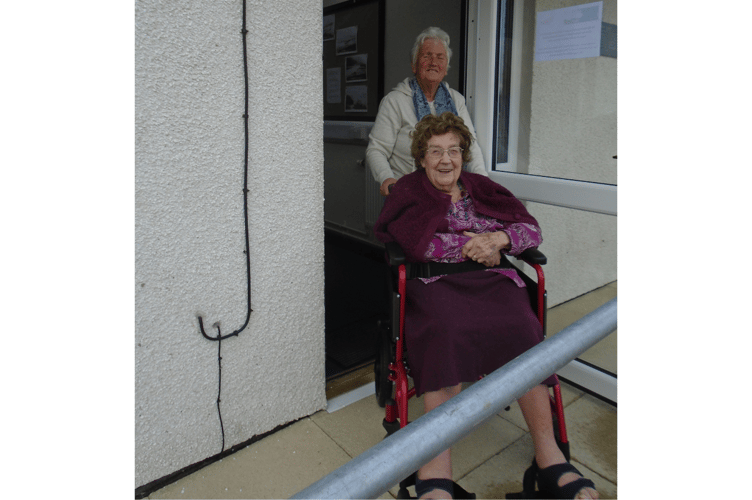 Win Jones is helped by Gwenda Griffiths onto one of the new ramps at Neuadd Gymuned Talsarnau