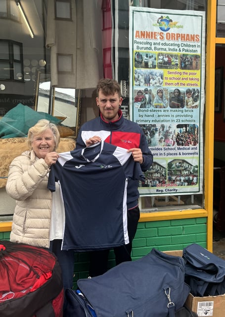Coleg Menai staff member Jamie Jones presenting Reverend Pauline Edwards with a football kit outside the Annie’s Orphans shop in Bangor