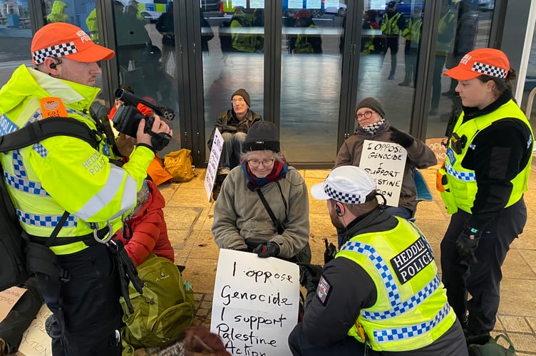 Machynlleth town councillor Ann MacGarry surrounded by police holding a sign which reads, 'I oppose genocide. I support Palestine Action'. Photo: Palestine Solidarity Aberystwyth