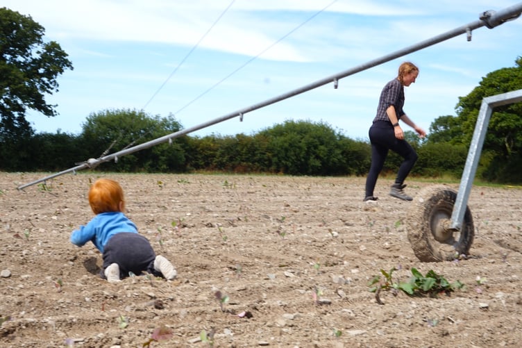 Katherine Langton with her one-year-old setting up the boom irrigator on a dry field.