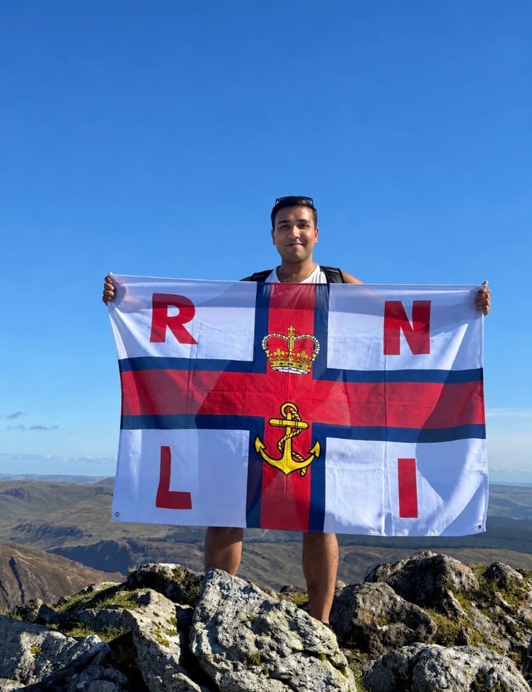 ScreenshotNishant Chandolia is pictured with an RNLI flag at the top of one of the four peaks of Cadair Idris